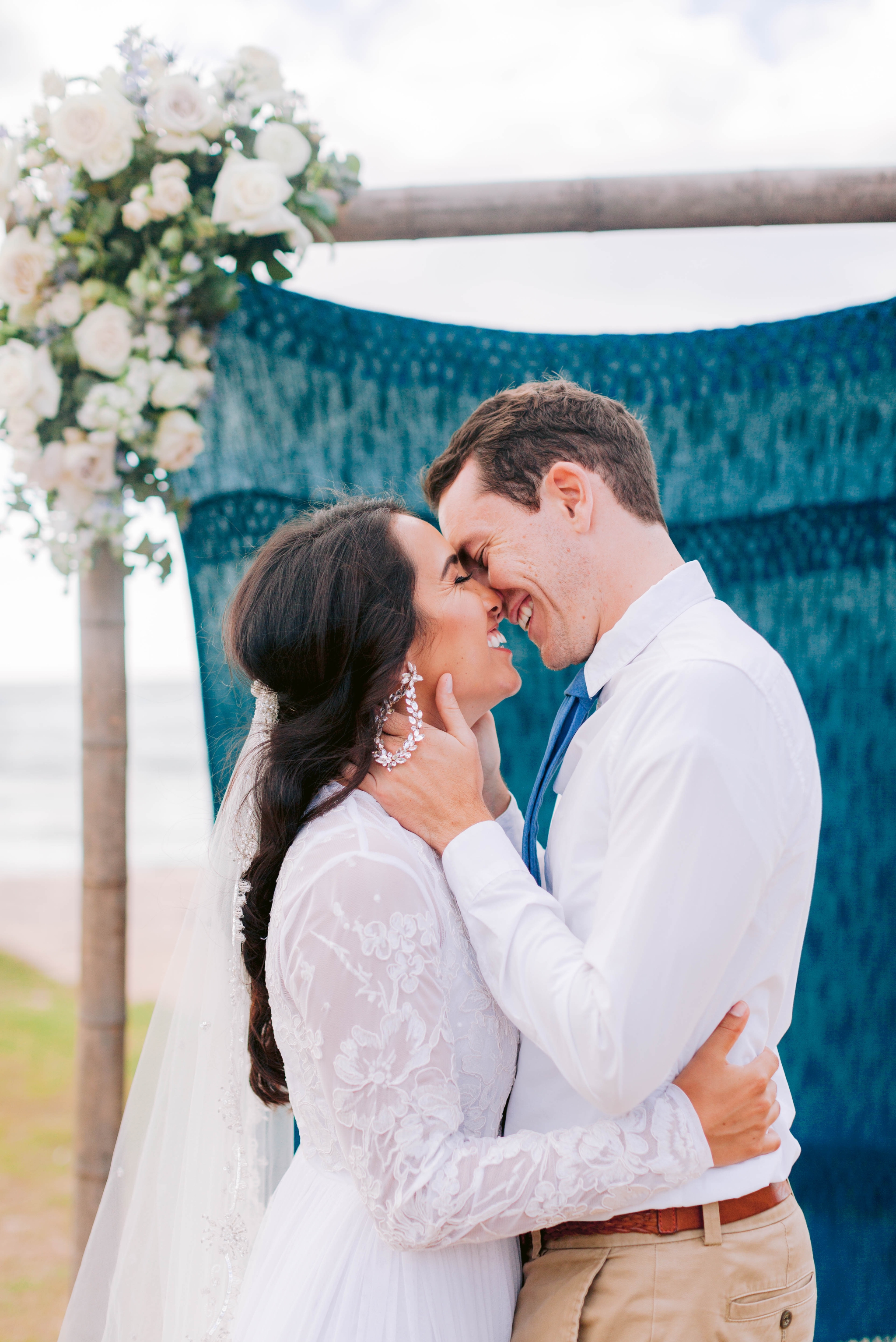 Bride + Groom kissing in front of a ceremony arch decorated with fabric and flowers - Ana + Elijah - Wedding at Loulu Palm in Haleiwa, HI - Oahu Hawaii Wedding Photographer 