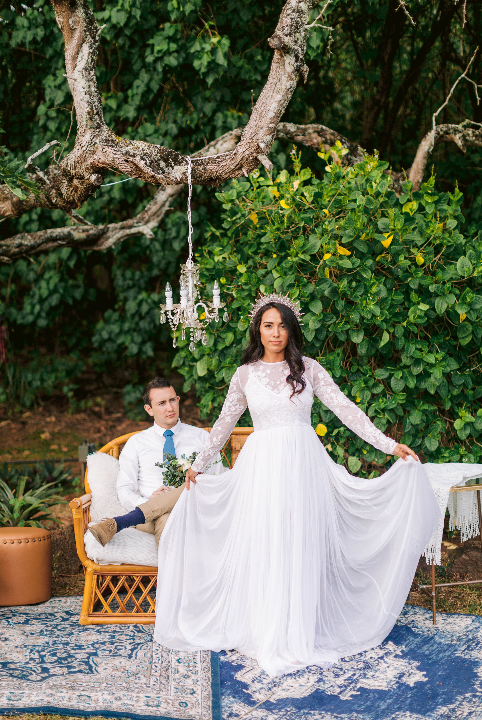  Bride and groom relaxing in an outdoor lounge with rattan furniture and blue rugs -  bride is wearing a wedding dress by asos and a crystal crown - Ana + Elijah - Wedding at Loulu Palm in Haleiwa, HI - Oahu Hawaii Wedding Photographer 