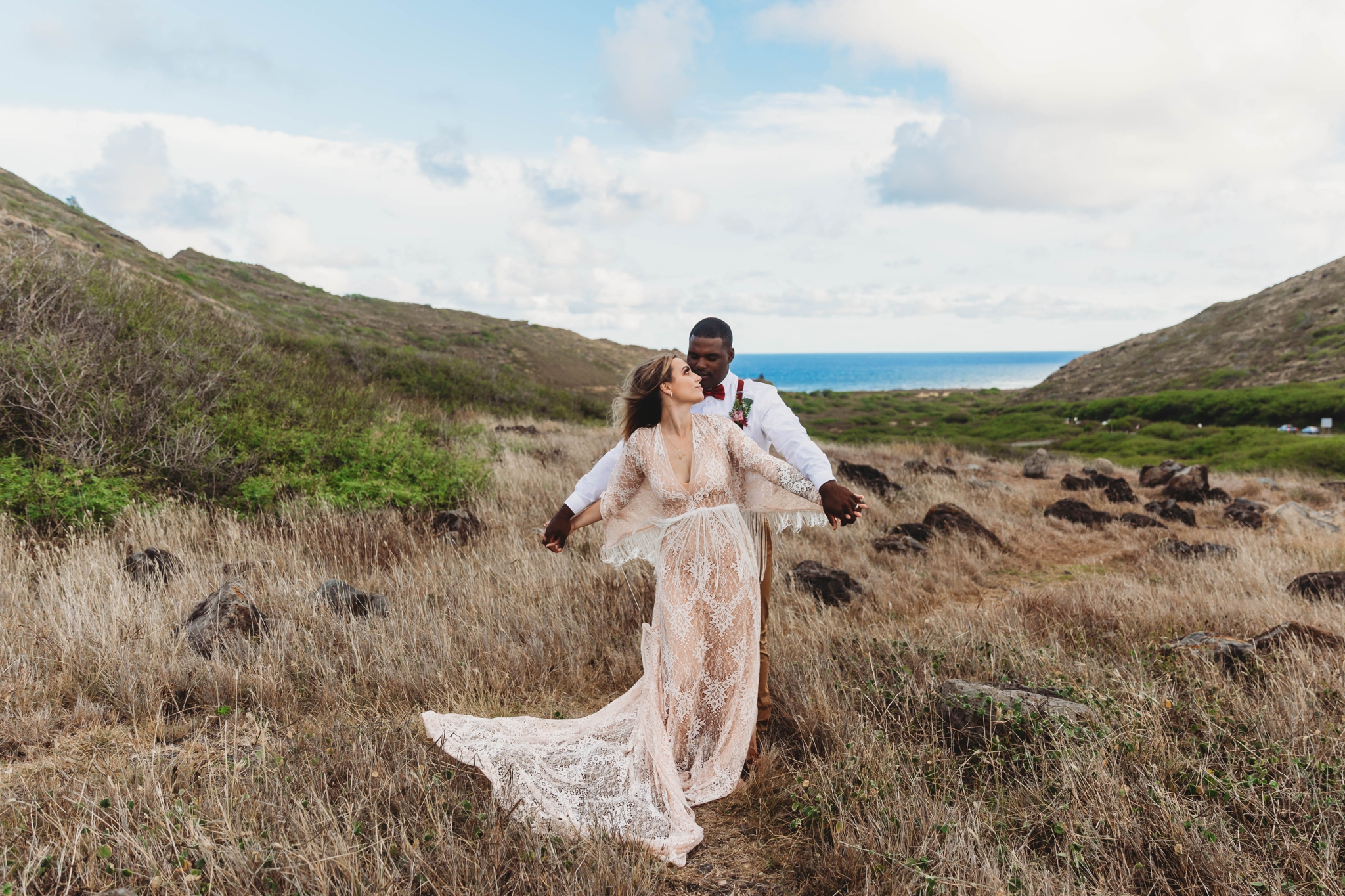  couple dancing around in the wind - Elopement at Makapuu Lookout, Waimanalo, HI - Oahu Hawaii Engagement Photographer - Bride in a flowy fringe boho wedding dress - in grassy mountains with the ocean in the back - lanikai lookout - deutsche hochzeit