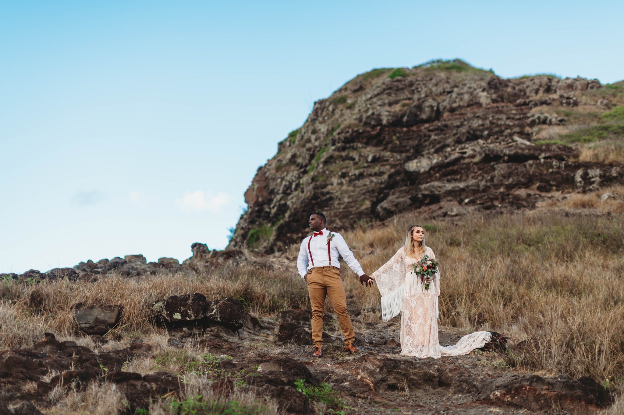  couple standing besides the cliffs - Elopement at Makapuu Lookout, Waimanalo, HI - Oahu Hawaii Engagement Photographer - Bride in a flowy fringe boho wedding dress - in grassy mountains with the ocean in the back - lanikai lookout - deutsche hochzei