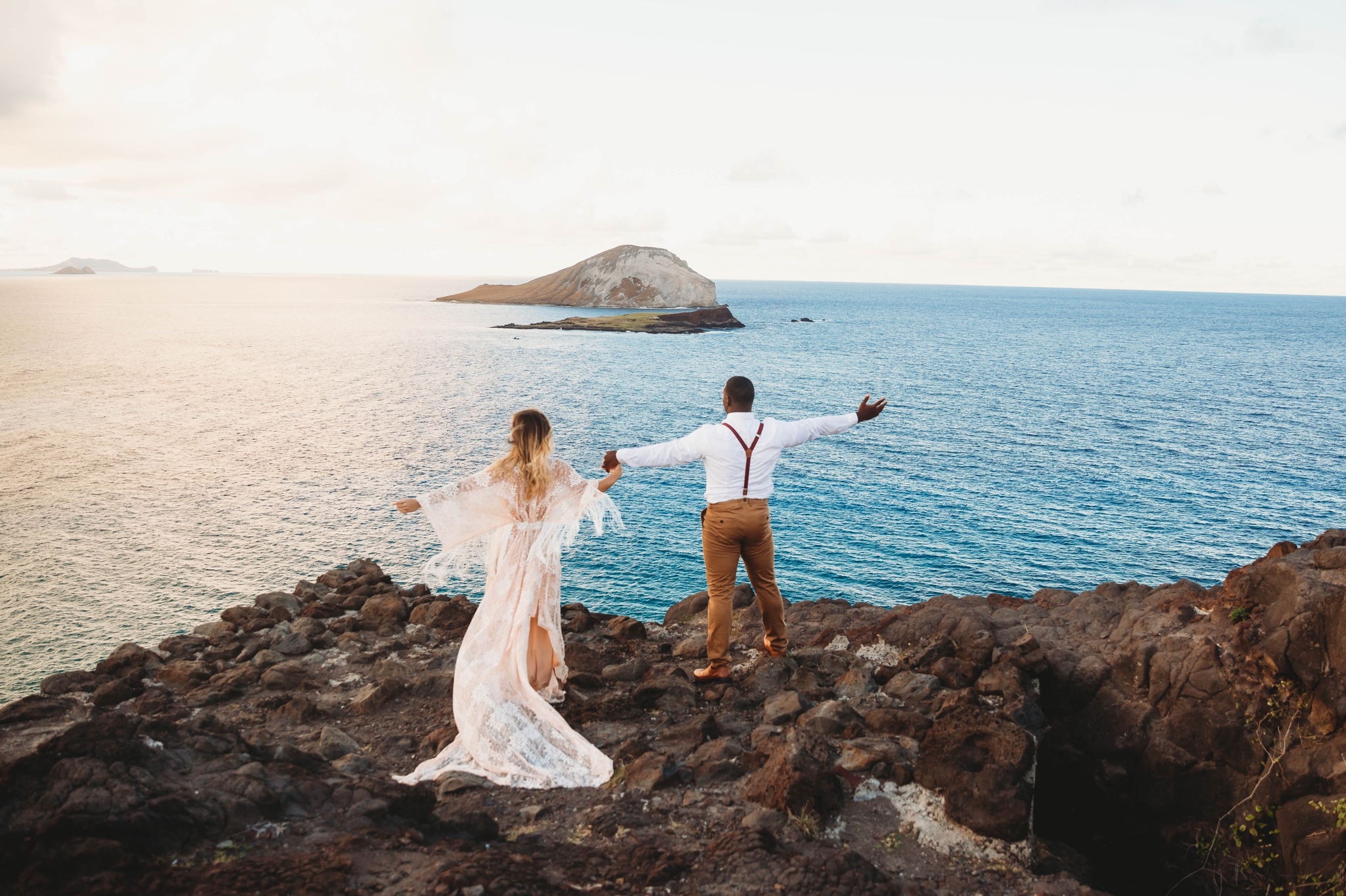  couple on the cliffs above Makapuu Beach at the Lookout, Waimanalo, HI looking over the ocean with the  Kāohikaipu Island in the background  - Oahu Hawaii Engagement Photographer - Bride in a flowy fringe boho wedding dress - lanikai lookout - deuts