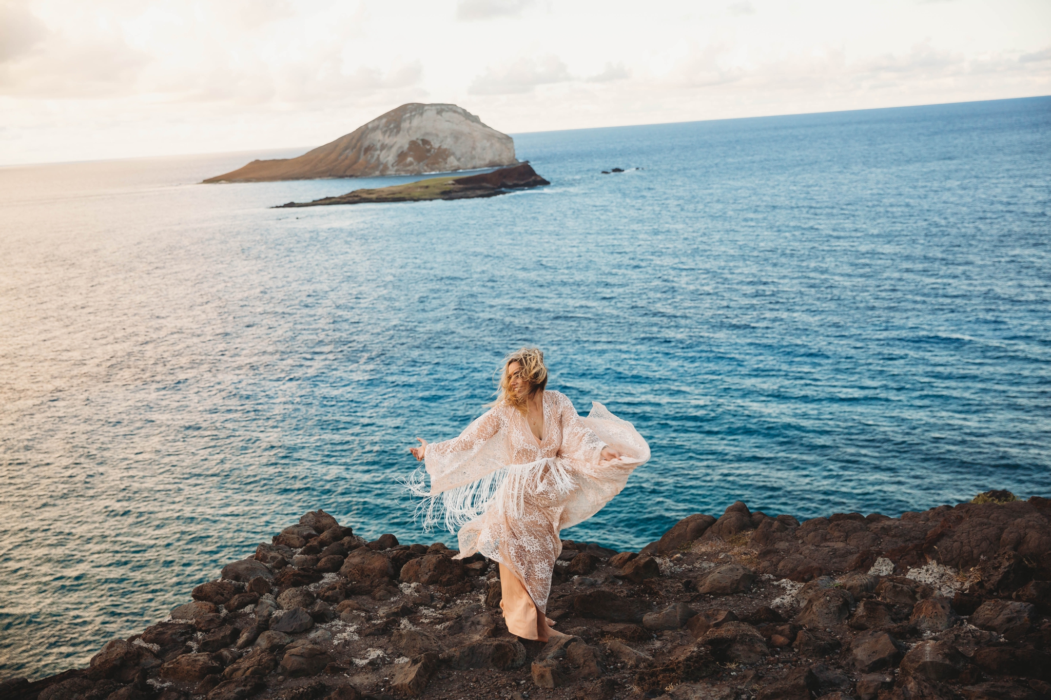  bride on the cliffs above Makapuu Beach at the Lookout, Waimanalo, HI looking over the ocean with the  Kāohikaipu Island in the background  - Oahu Hawaii Engagement Photographer - Bride in a flowy fringe boho wedding dress - lanikai lookout - deutsc