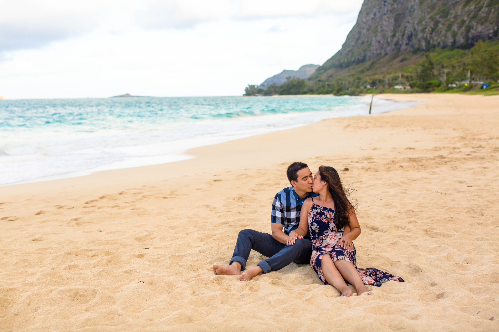 engagement photography session at waimanalo beach park - couple is sitting in the sand with the ocean and the mountains in the back ground - oahu hawaii wedding photographer