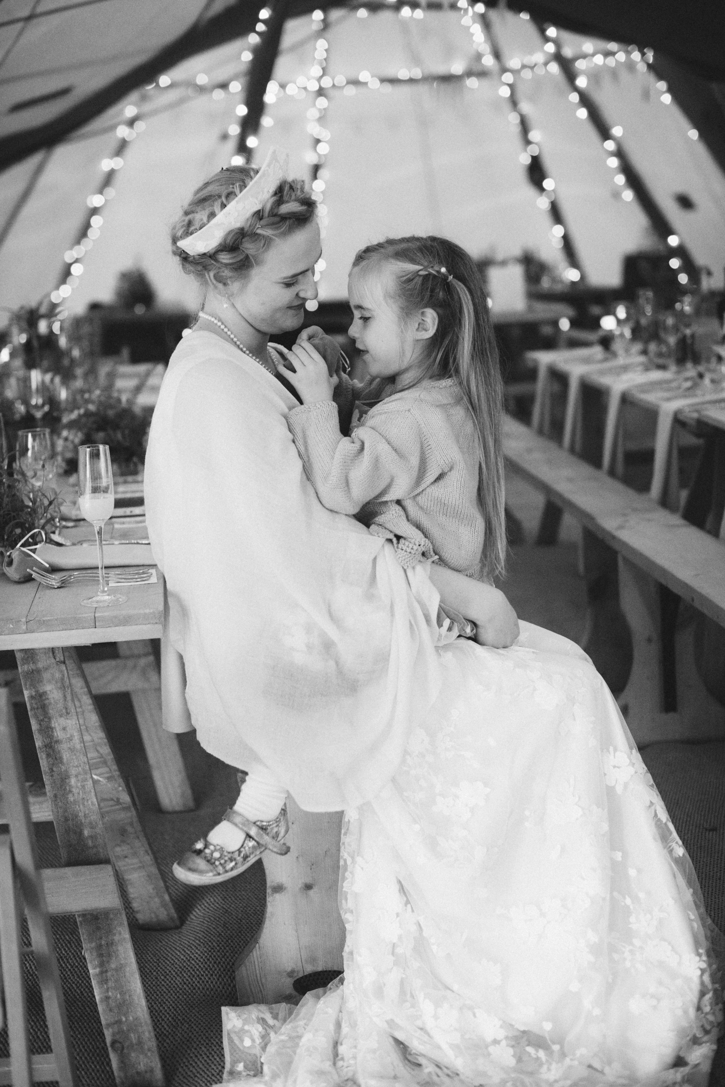 black and white photography inside a woodland wedding tipi with bride and flower girl sharing a hug