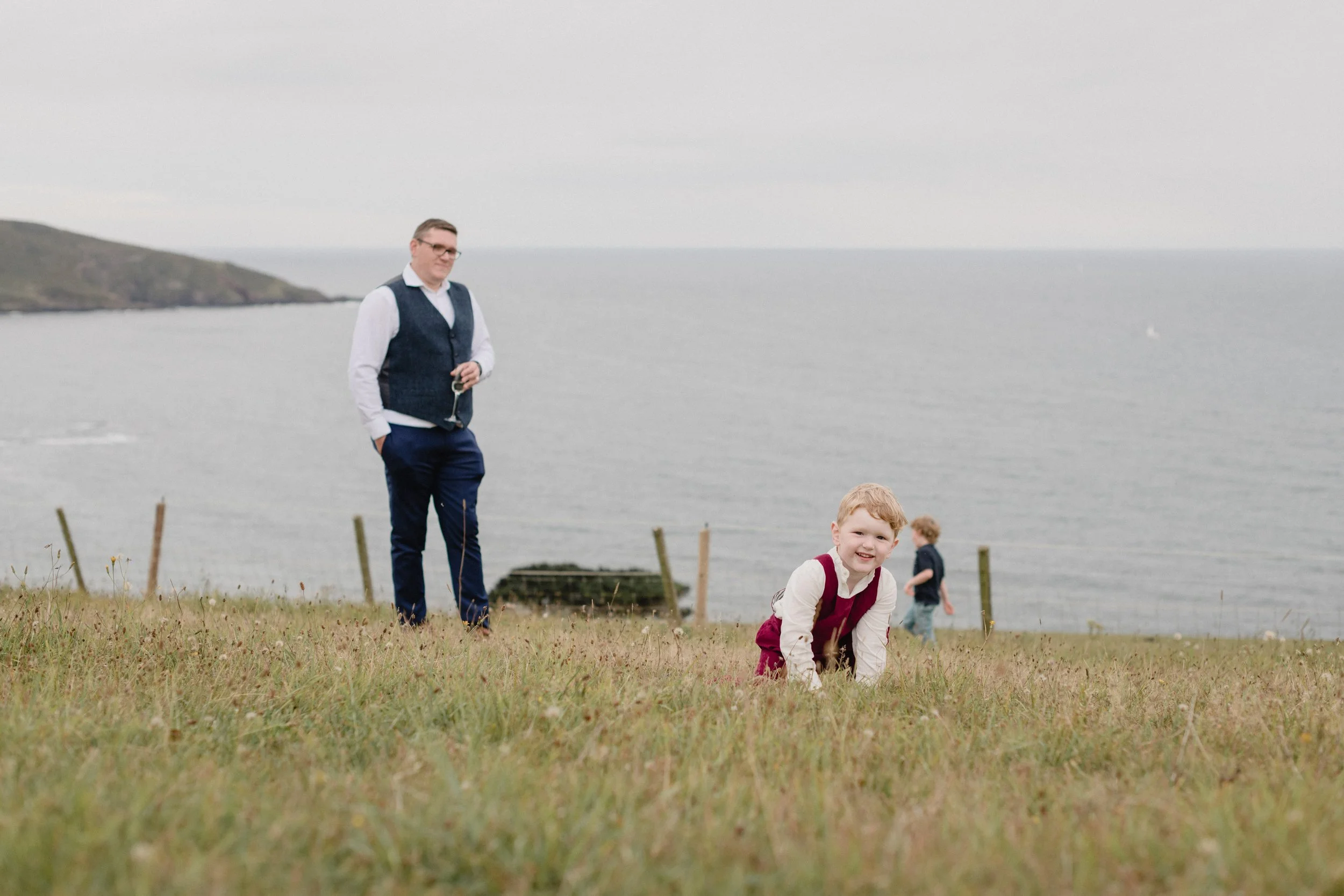 fun and candid alternative wedding photographers of children playing in the meadow overlooking the sea