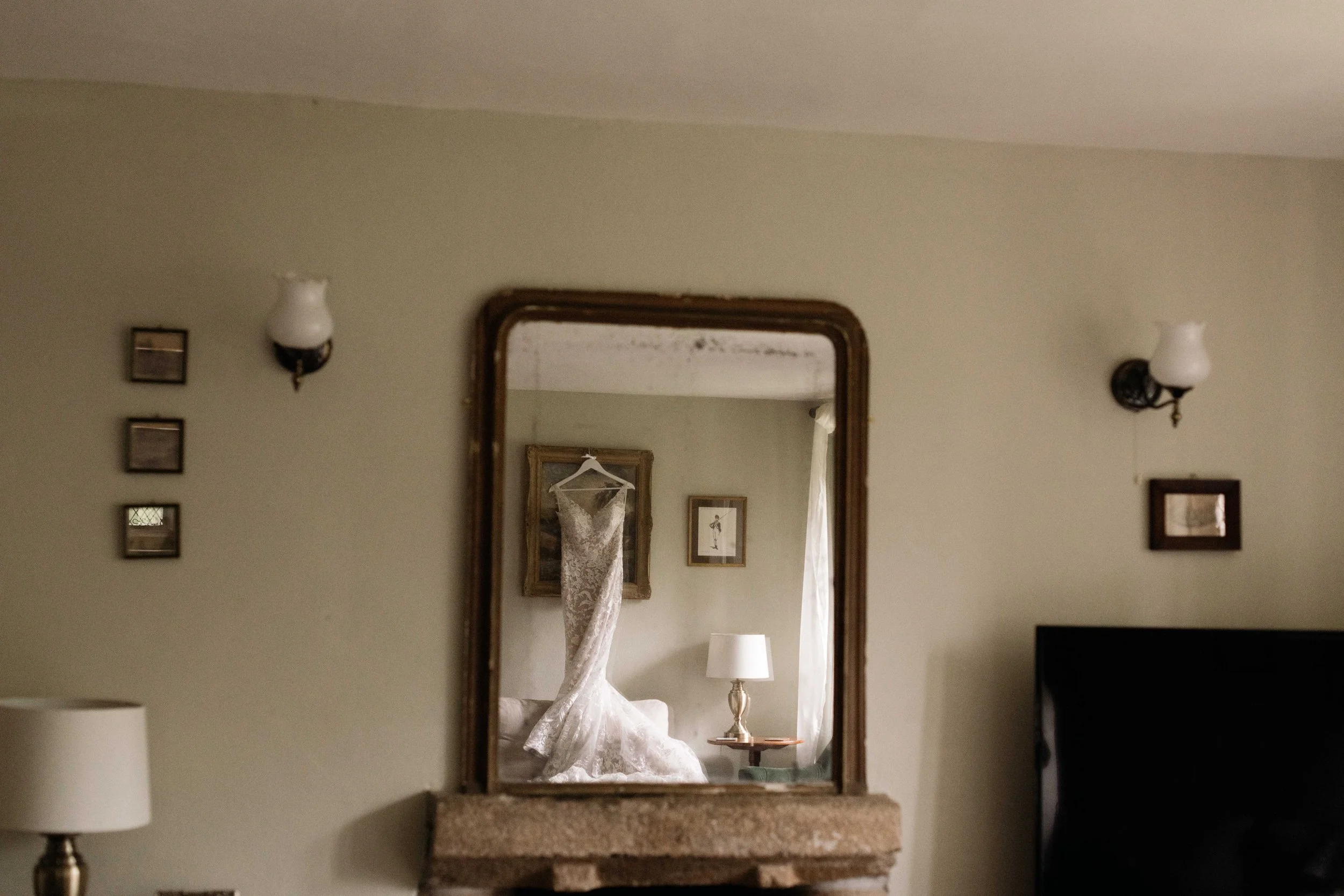 lacy romantic wedding dress hanging up in the tudor manor at Pengenna Manor wedding venue captured by alternative wedding photographers in Cornwall