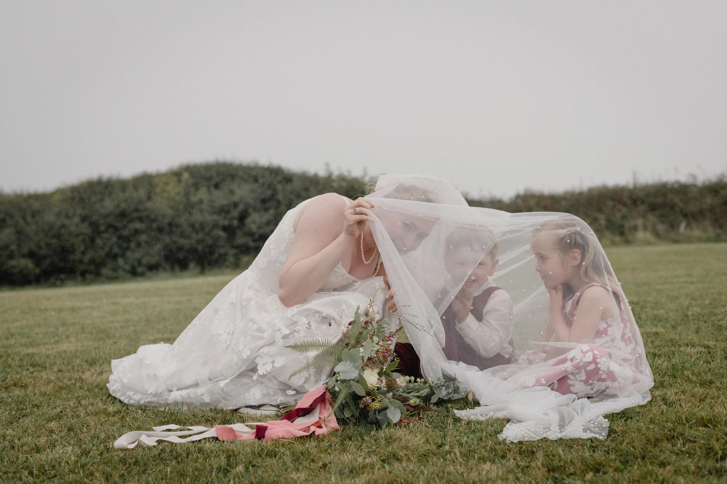 page boy and flower girl hiding under the brides veil