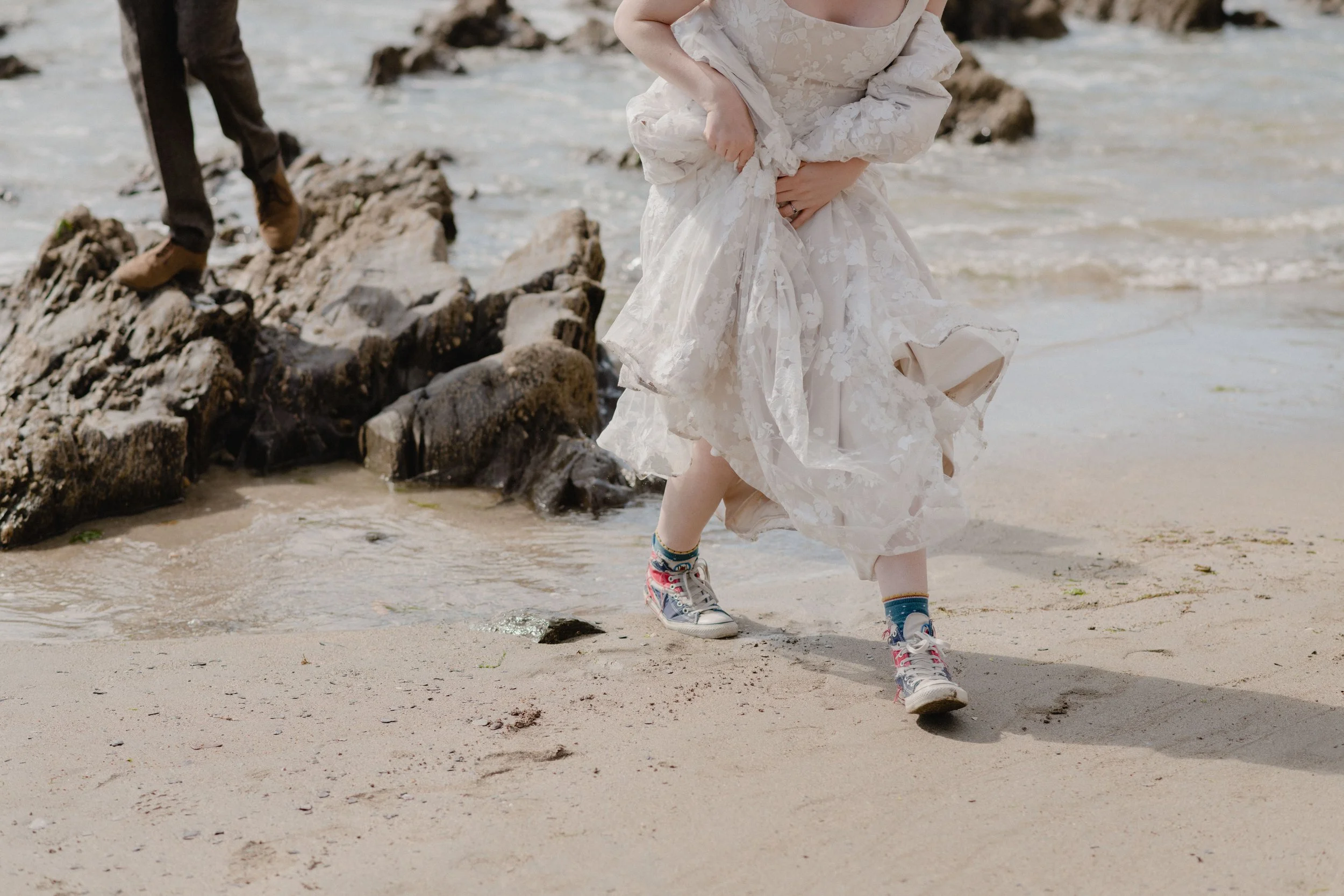 bride in union jack converse and romantic lace blush wedding dress with square neckline by the sea