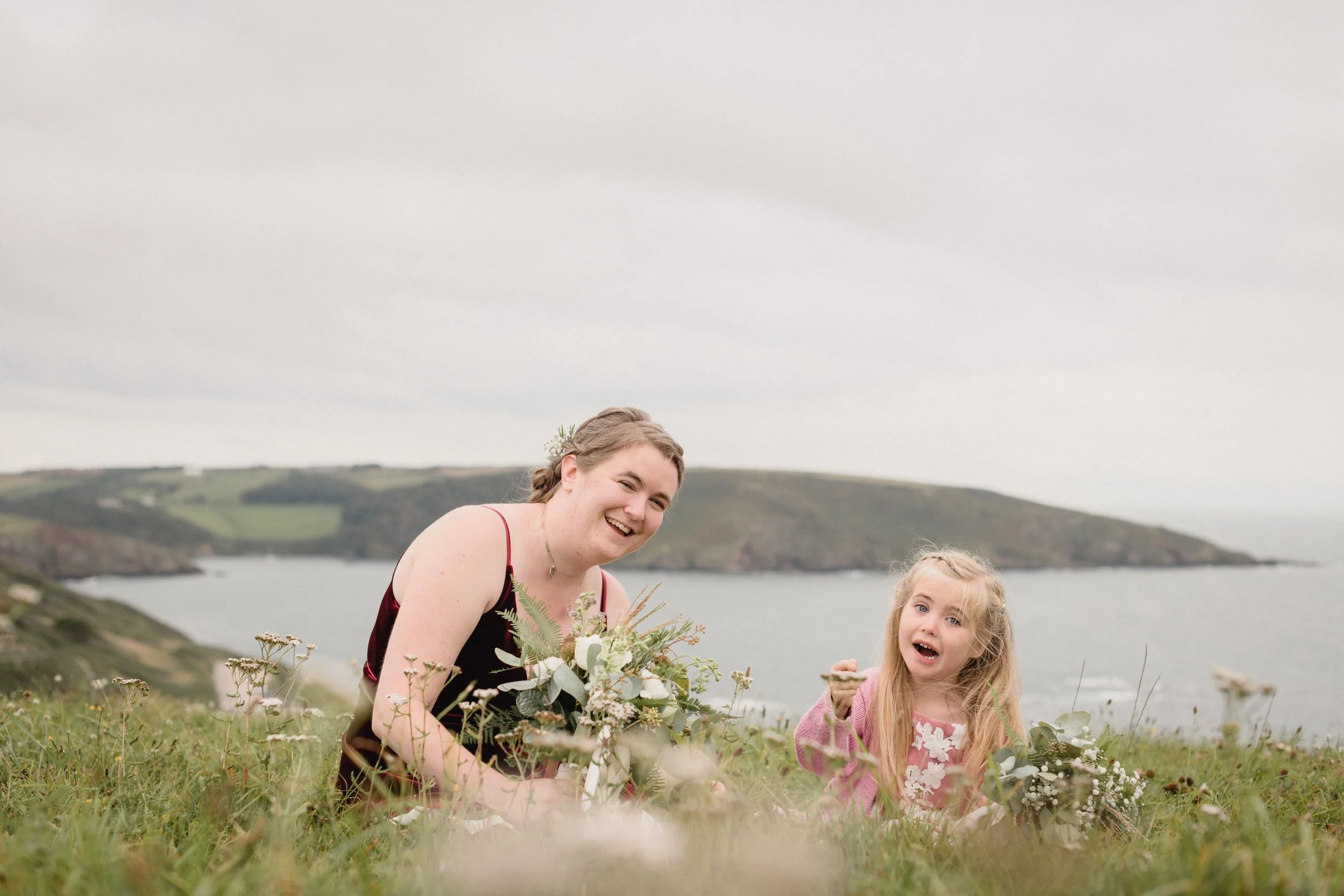 sweet and romantic whimsical wedding portraits of bridesmaids sitting in the wildflowers overlooking the ocean