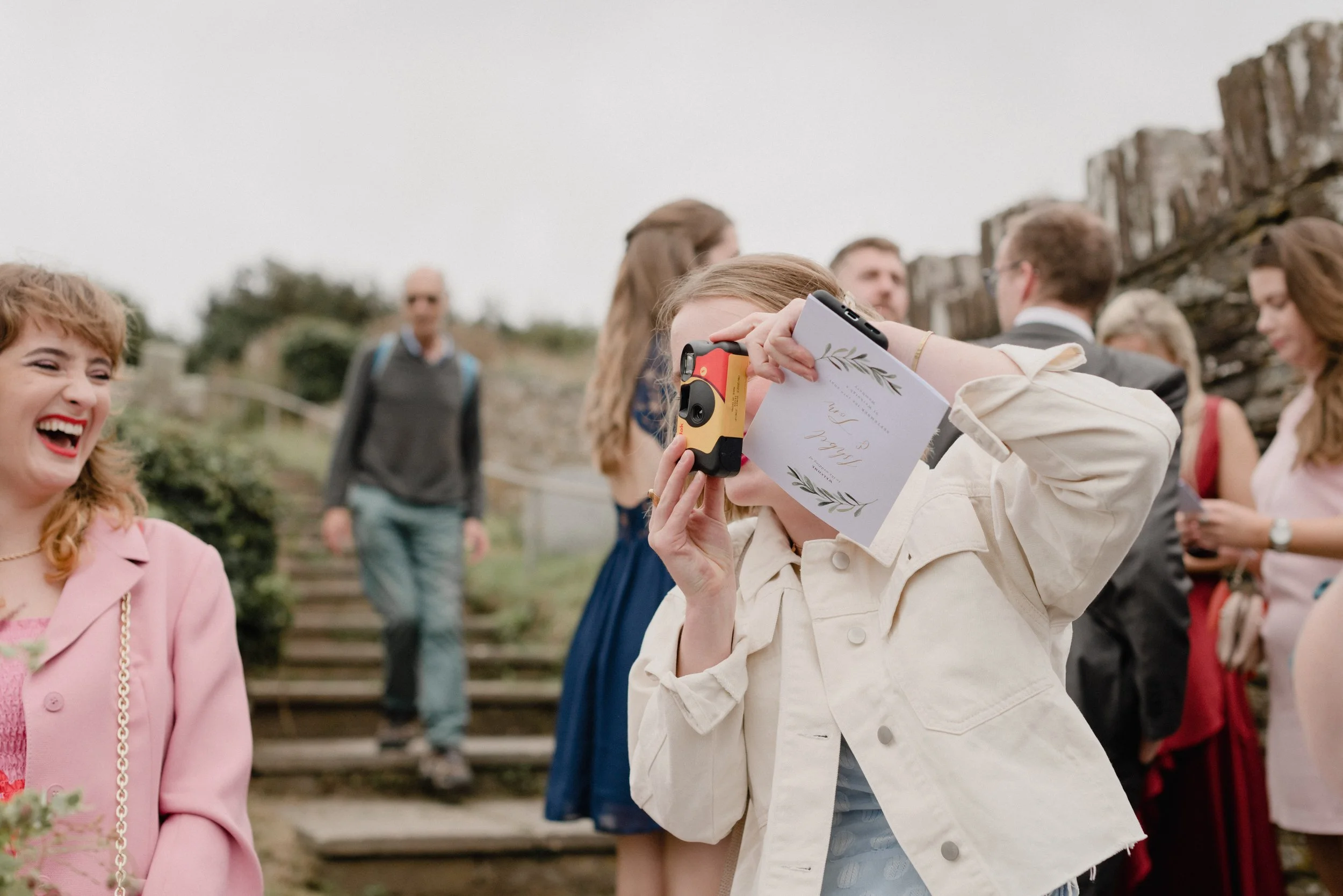 alternative reportage wedding photography of candid guest moments as girl captures wedding on disposable analogue film camera