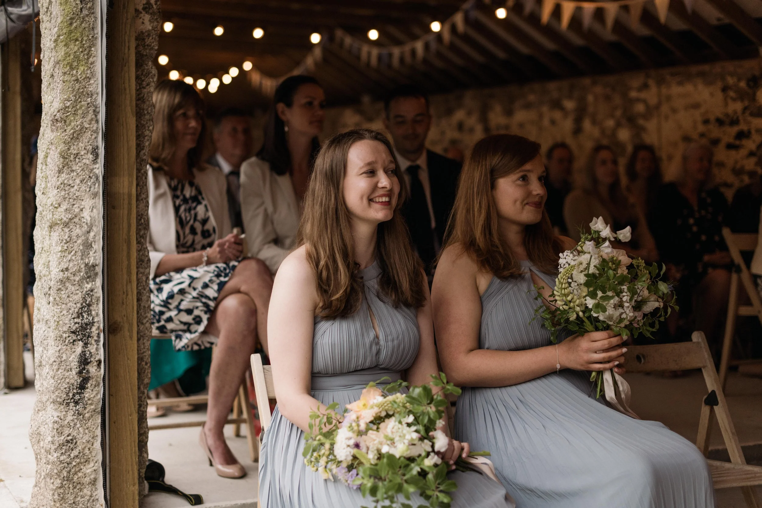 reportage photography of bridesmaids watching a wedding ceremony at pengenna manor's stone barn