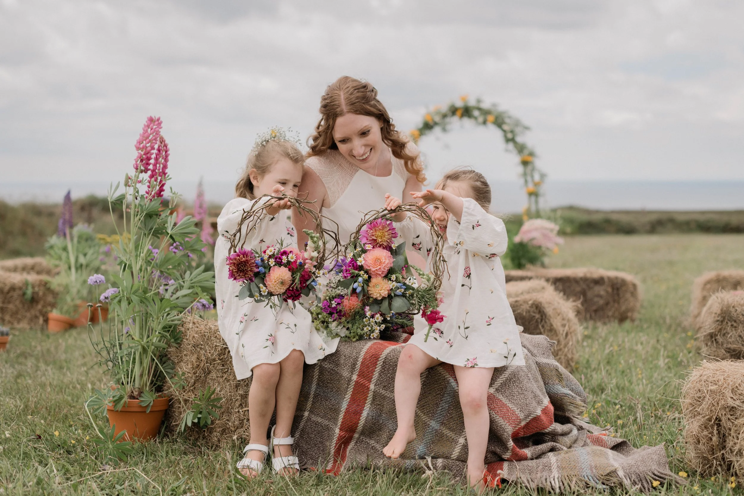 bride and bridesmaids together with floral hoops at St Agnes wedding field for her boho wildflower wedding