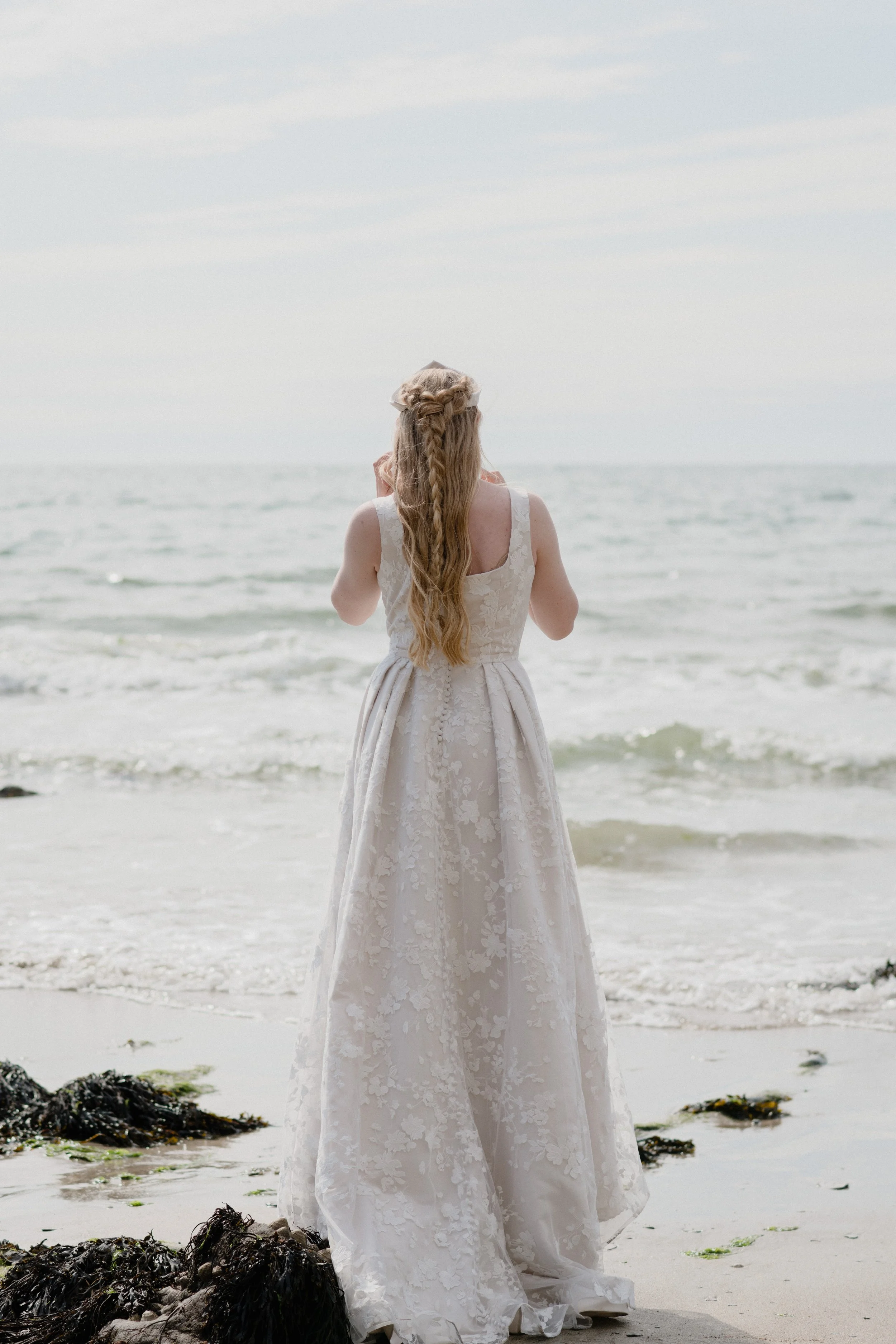 blush lace bridal inspiration for this fairytale Elin gown with lord of the rings inspired Elf queen hair and russian koshonik bridal accessories against the aquamarine ocean