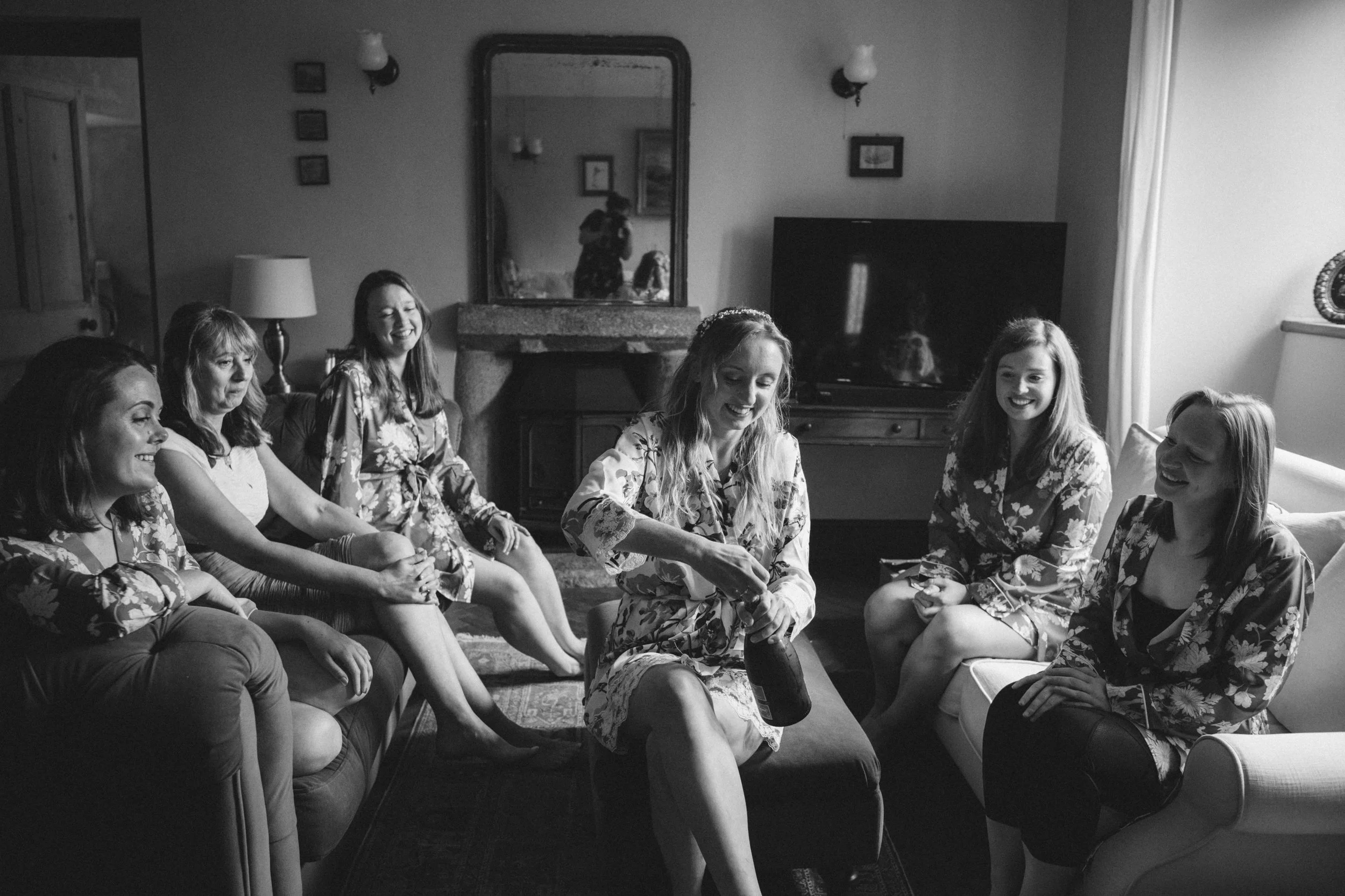 bride and her bridesmaids crack open the champagne a scene in black and white natural documentary photography