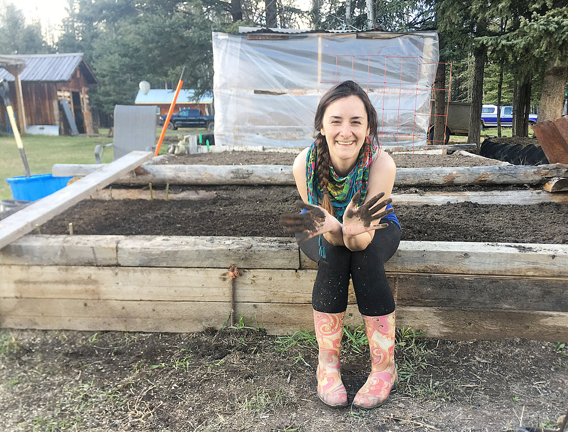 在休息旁边，在她的升降床上花园旁边，蒂芙尼横穿，首次公民科学队参与者，展示了她的土壤覆盖的手。