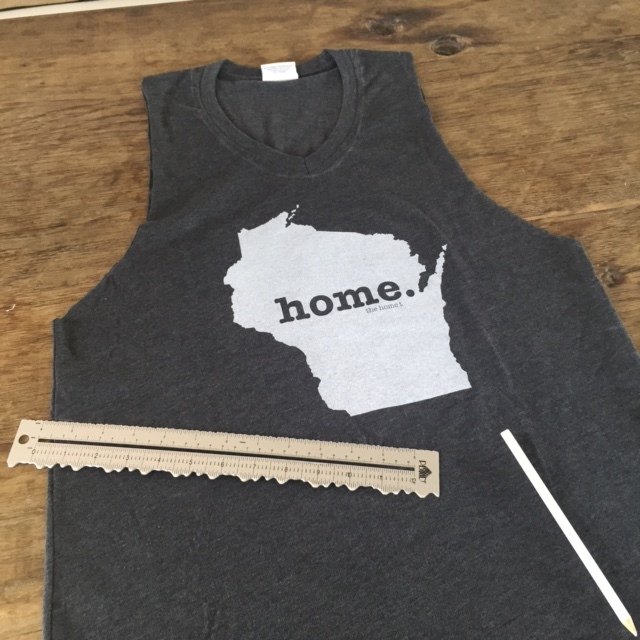 Lay your tee perfectly flat on a table so the front and back line up perfectly. I started out by measuring and using the pencil to sketch lines as guides where I wanted to cut off the sleeves. Then I cut off the sleeves because I did this project on a hot 91 degree day. You can see that I cut the sleeves a little larger than the actual arm hole to give the tee shirt more of a drape effect. Keep in mind that with this large of a drape, you will need to layer and wear a tank underneath which was the look I was going for, but you can experiment with this step. I also drew in white pencil a guide around the v-neck where I would trim this off too. After you cut the tee shirt, give the edges a simple little pull or tug to straighten the cuts. This also gets the edges to roll nicely. Then, where the ruler is, I began drawing a slight subtle "v" shape below the state that is centered on the tee. This will become my guide for the fringe. I thought this "v" gave it an unexpected shape and interest instead of just doing it straight across. But you could do it either way! Use your imagination!