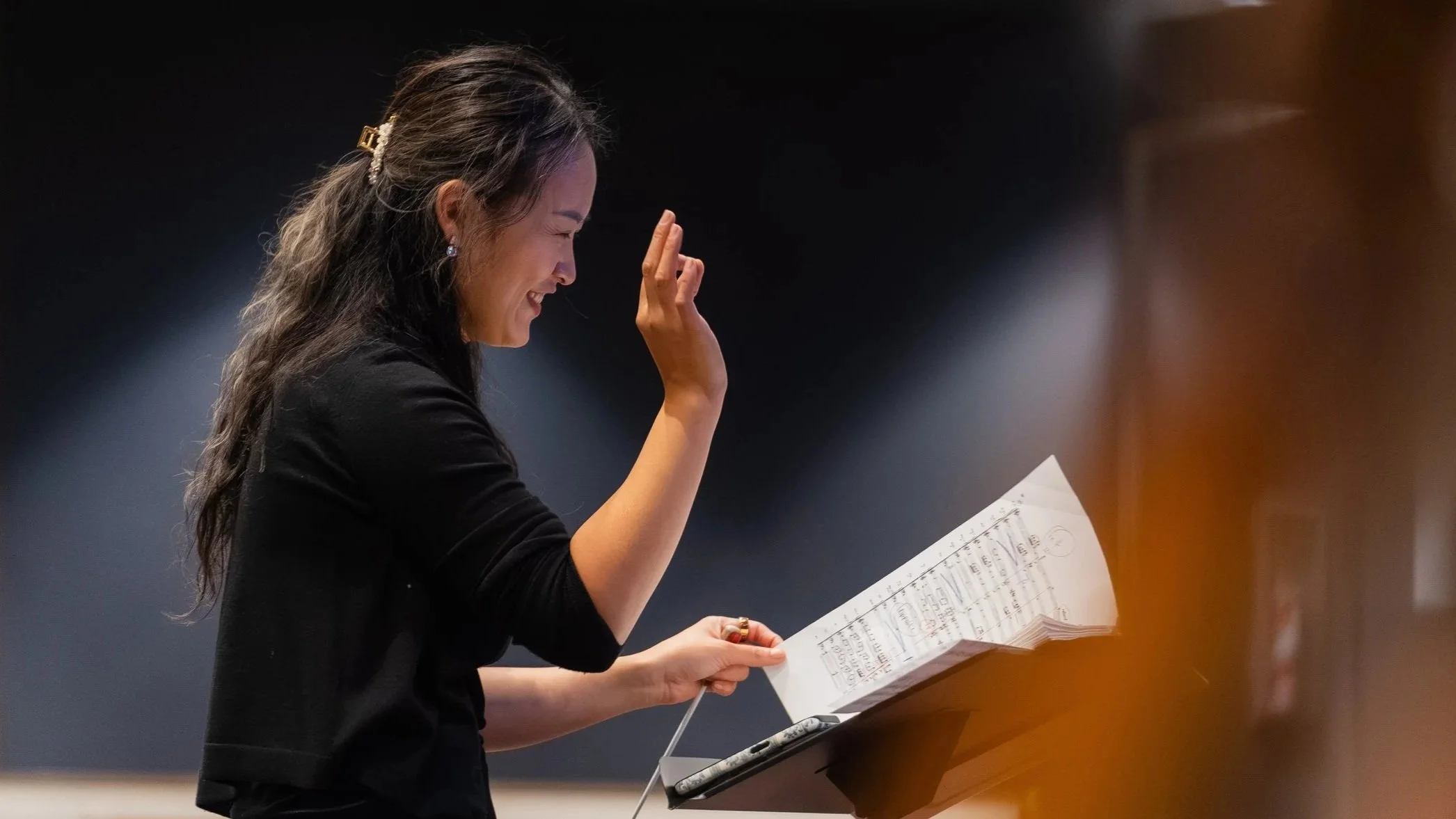 Conductor Yuchi Chou smiles while looking at a score