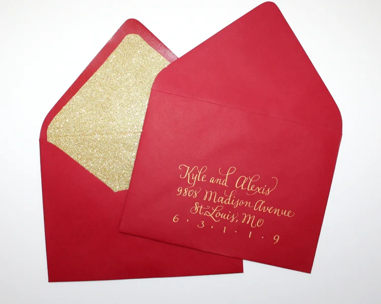 Bright red paper source envelopes, gold glitter liners, finished with custom hand lettered gold metallic addresses