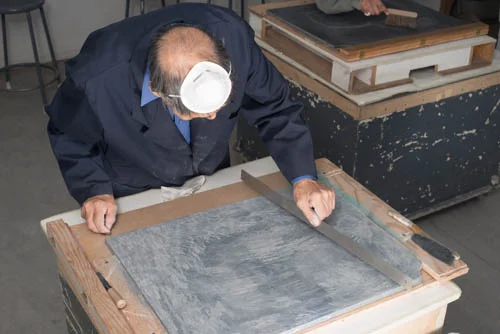 Qiatsuq was once a lithography printer so he understands the importance of keeping his options open. Here he uses a steel rule to check the level on the surface of the stone block before he stops using the chisel and turns to graining the stone prior to laying out his next project.