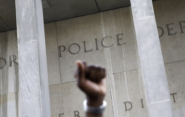 A protester raises his fist outside the Baltimore Police Department’s Western District police station during a march and vigil for Freddie Gray last Tuesday. Gray died of a spinal injury April 19 while he was in police custody. (AP / Patrick Semansky)