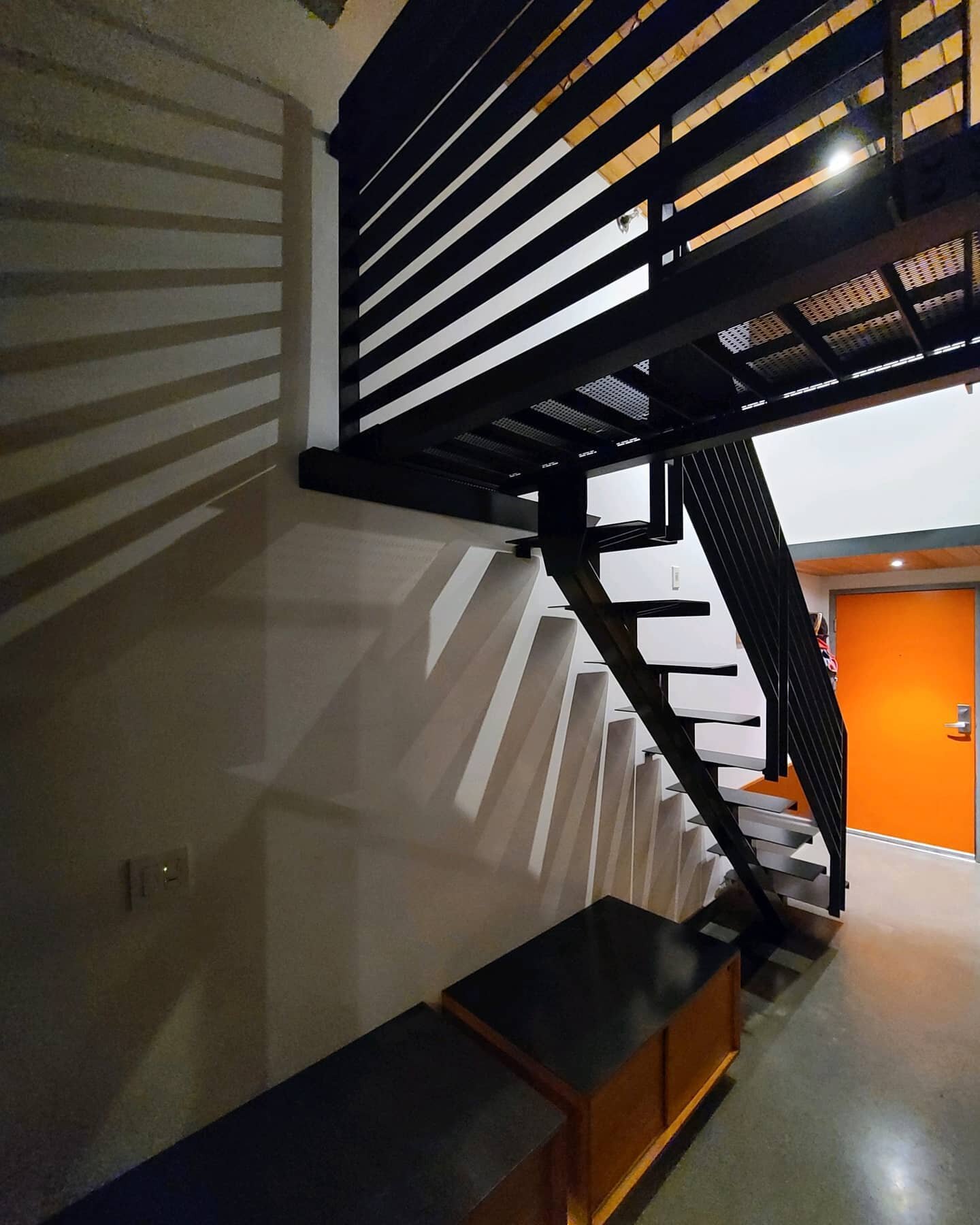 Steel mono stair system, installed. Details: floating mono stringer with hidden mechanical connections, profiled non-slip steel treads with open risers (grip to come), adjoining catwalk with perforated floor, side-mounted rails wrapped up and around.