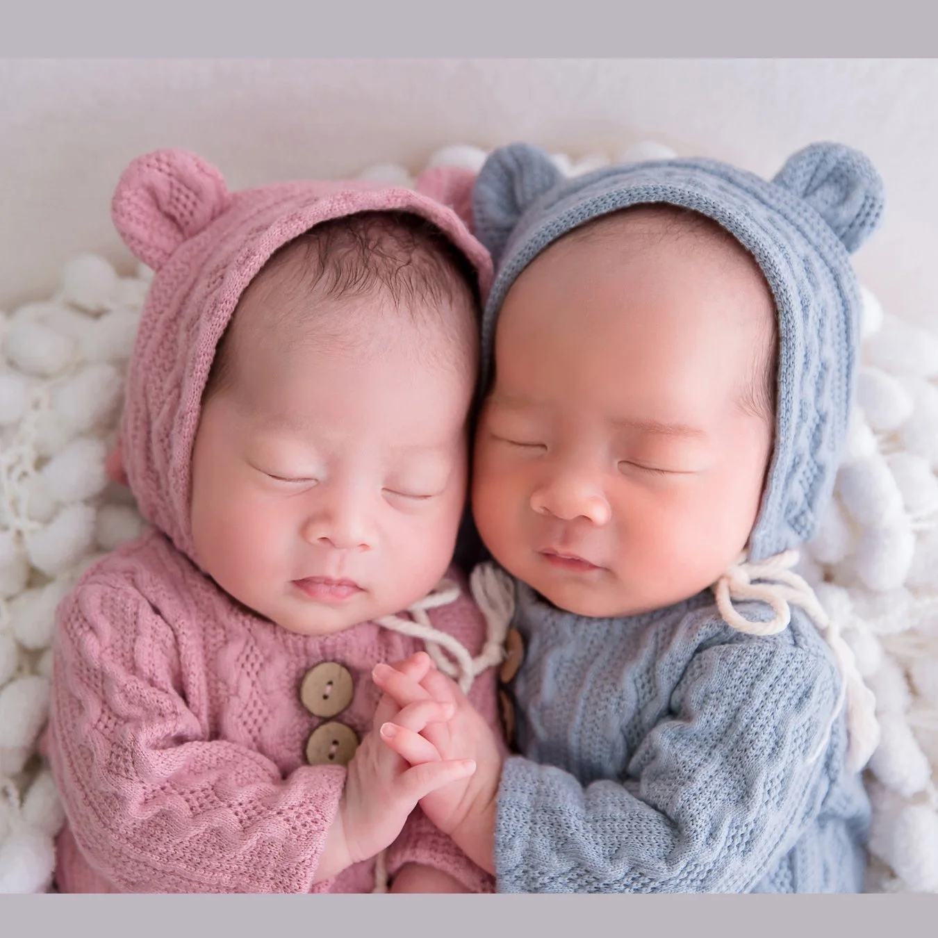 Sleeping newborn twins wearing pink and grey knitted bear bonnets