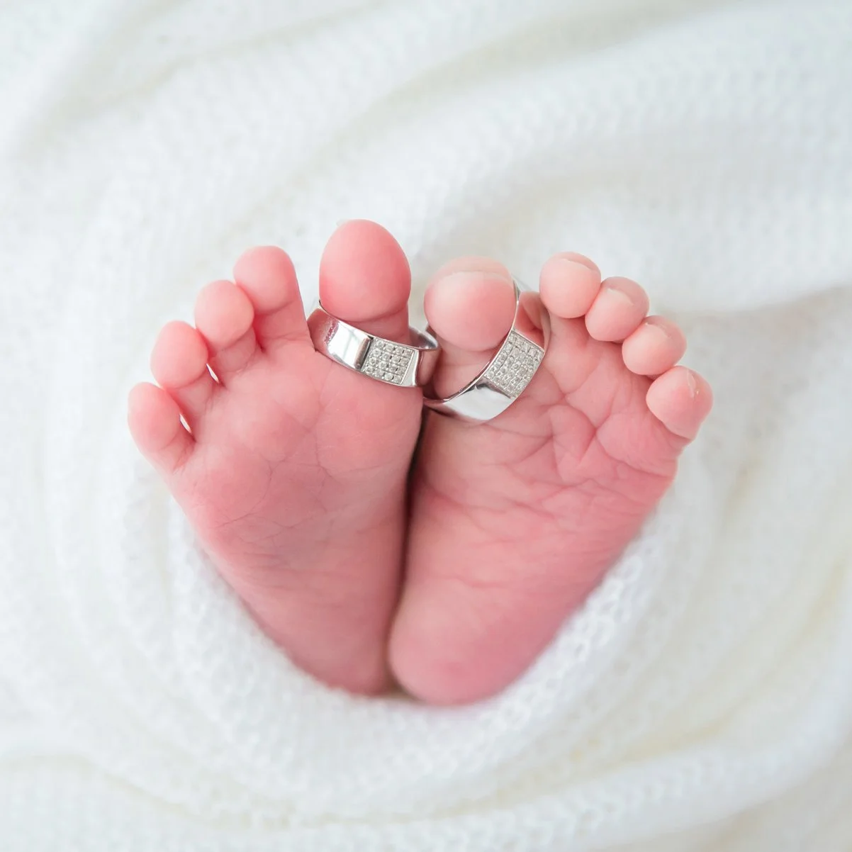 Close-up of tiny newborn feet with two wedding rings resting across the toes on a white blanket