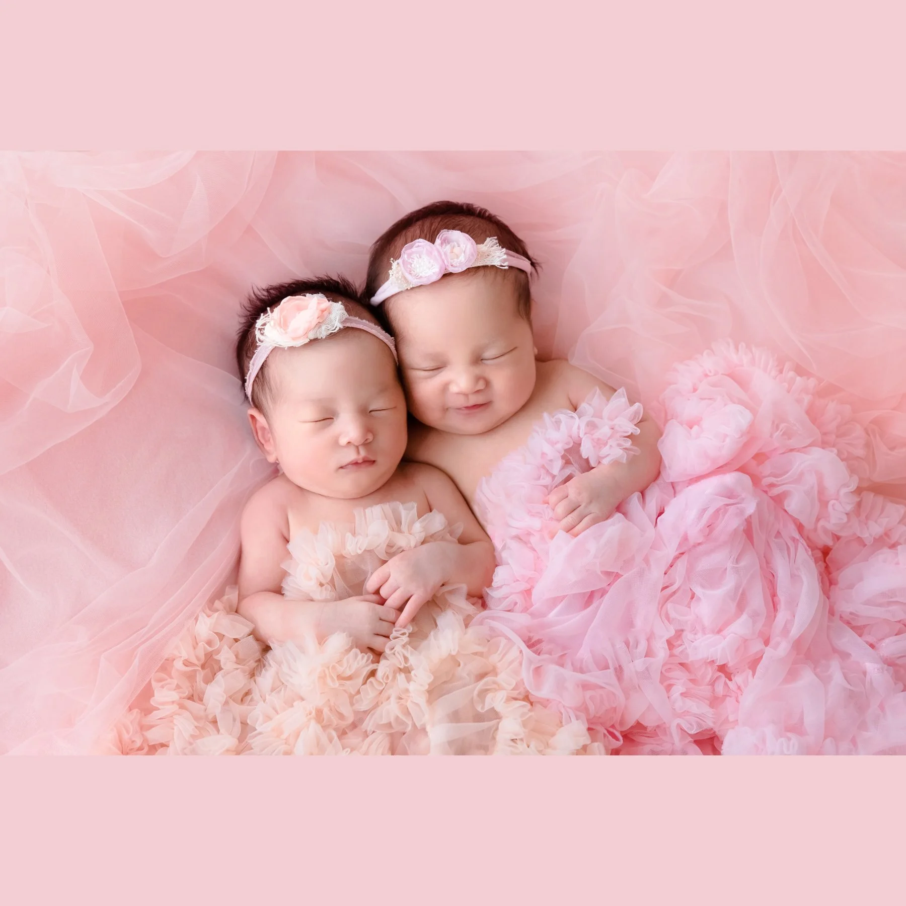 Newborn twins wearing pink floral outfits and matching headbands