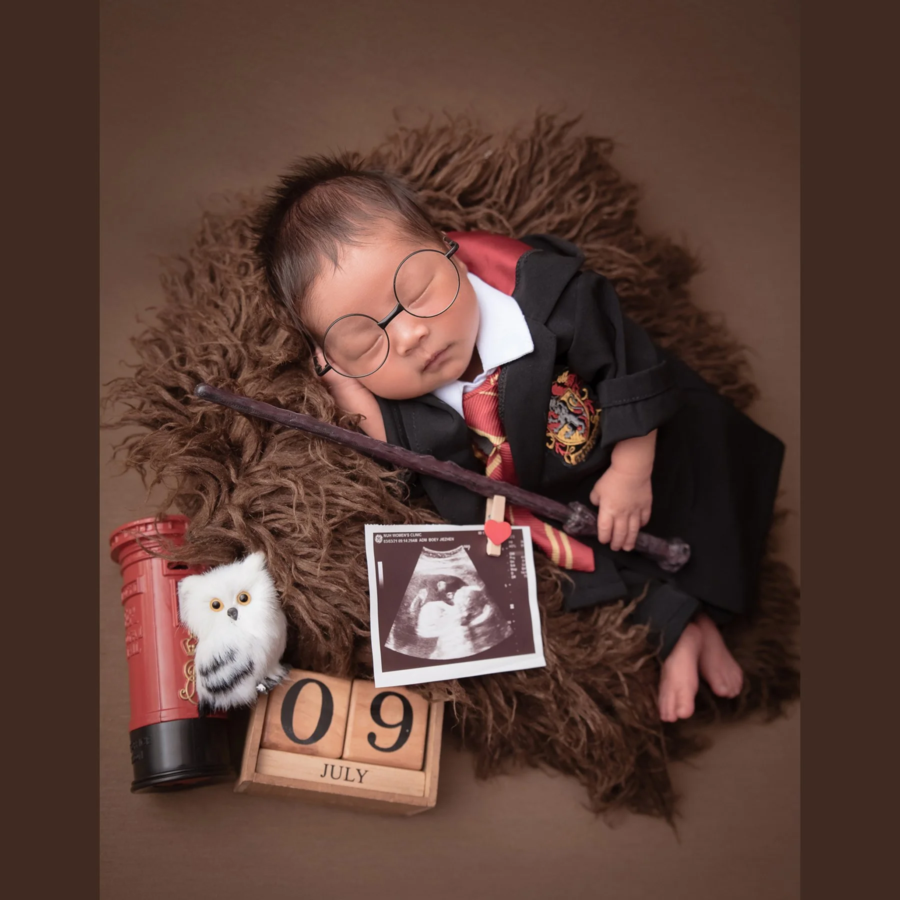 Sleeping newborn dressed as Harry Potter with round glasses, a wand and owl toy on brown fur