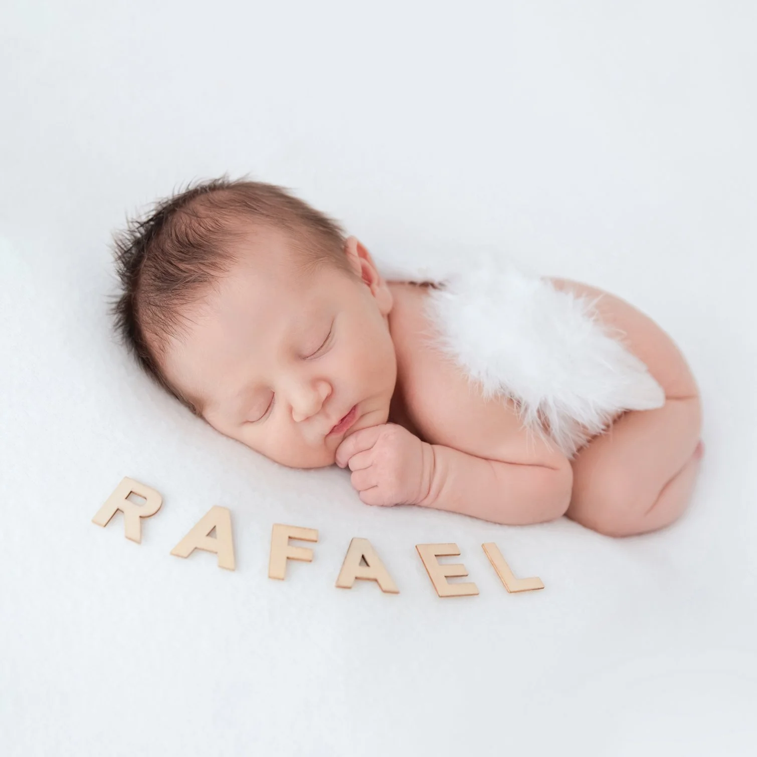 Sleeping newborn with white feathered angel wings resting on the tummy with hands under one cheek against white