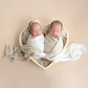Sleeping newborn twins wrapped in cream blankets in a heart-shaped basket