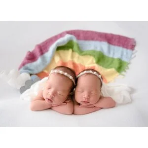 Sleeping newborn twins lying together beneath a knitted rainbow