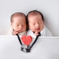 Newborn twins resting behind a camera with a red heart between them