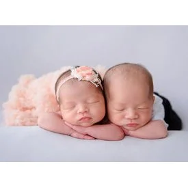 Sleeping newborn twins lying side by side with one wearing a pink floral headband