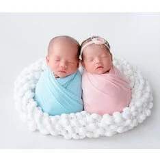 Newborn twins wrapped in blue and pink blankets in a white woven basket