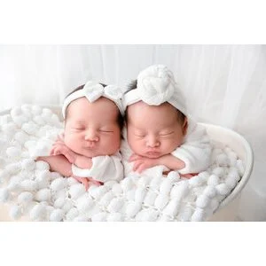 Sleeping newborn twins wearing white bows and cream knitted outfits