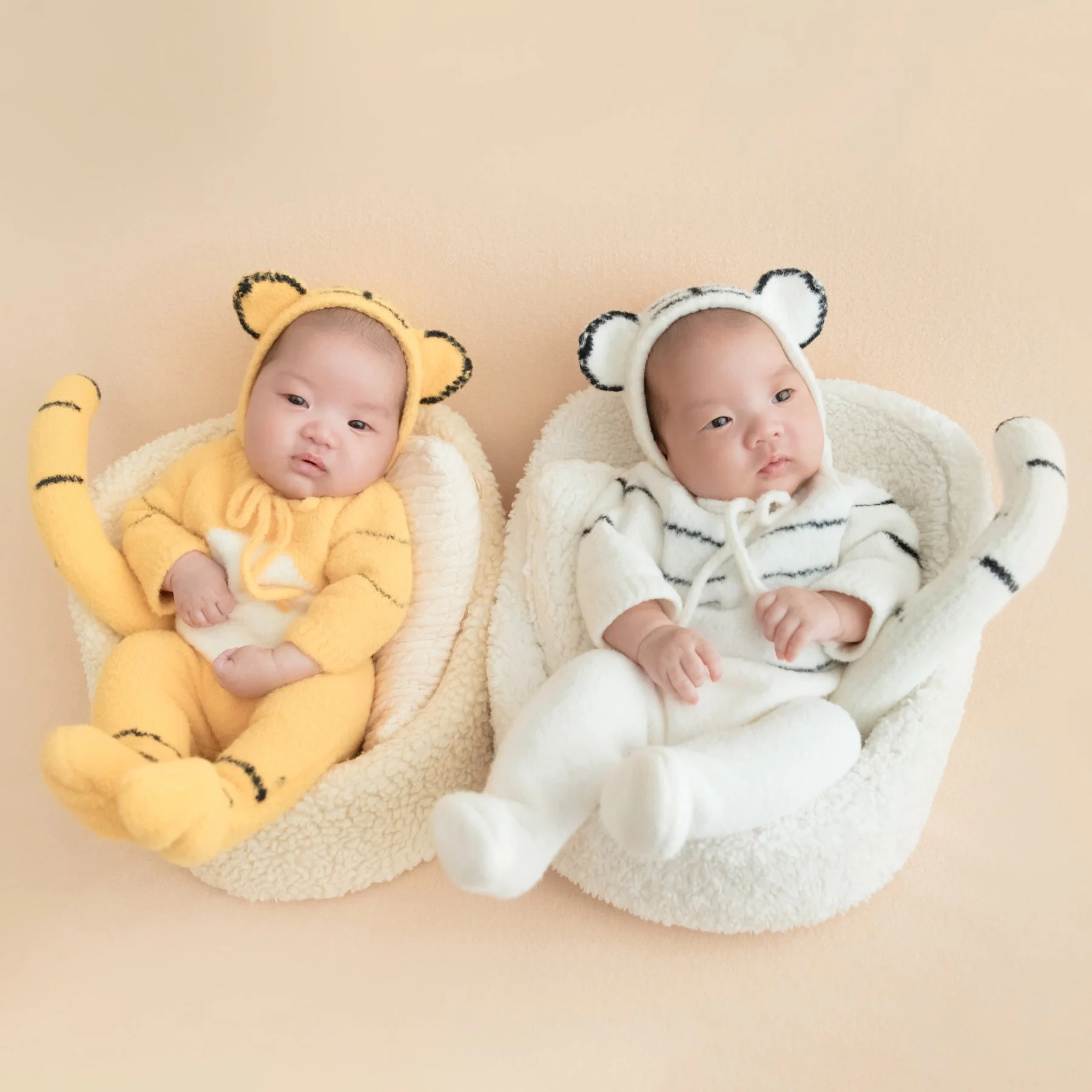 Newborn twins wearing yellow and white bear outfits in matching miniature chairs