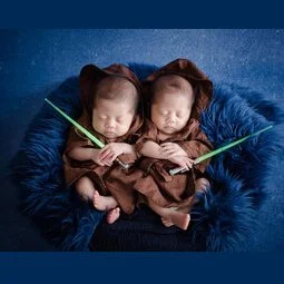 Newborn twins dressed as Jedi with miniature green lightsabers against a blue backdrop