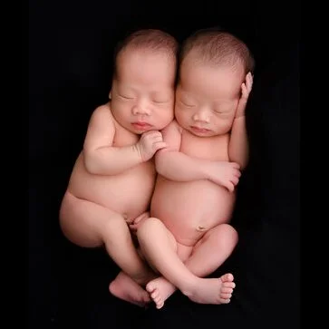 Sleeping newborn twins curled together against a black background