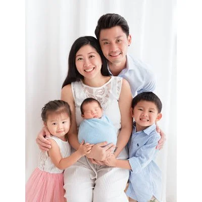 Parents posing with their blue-wrapped newborn and two smiling older siblings