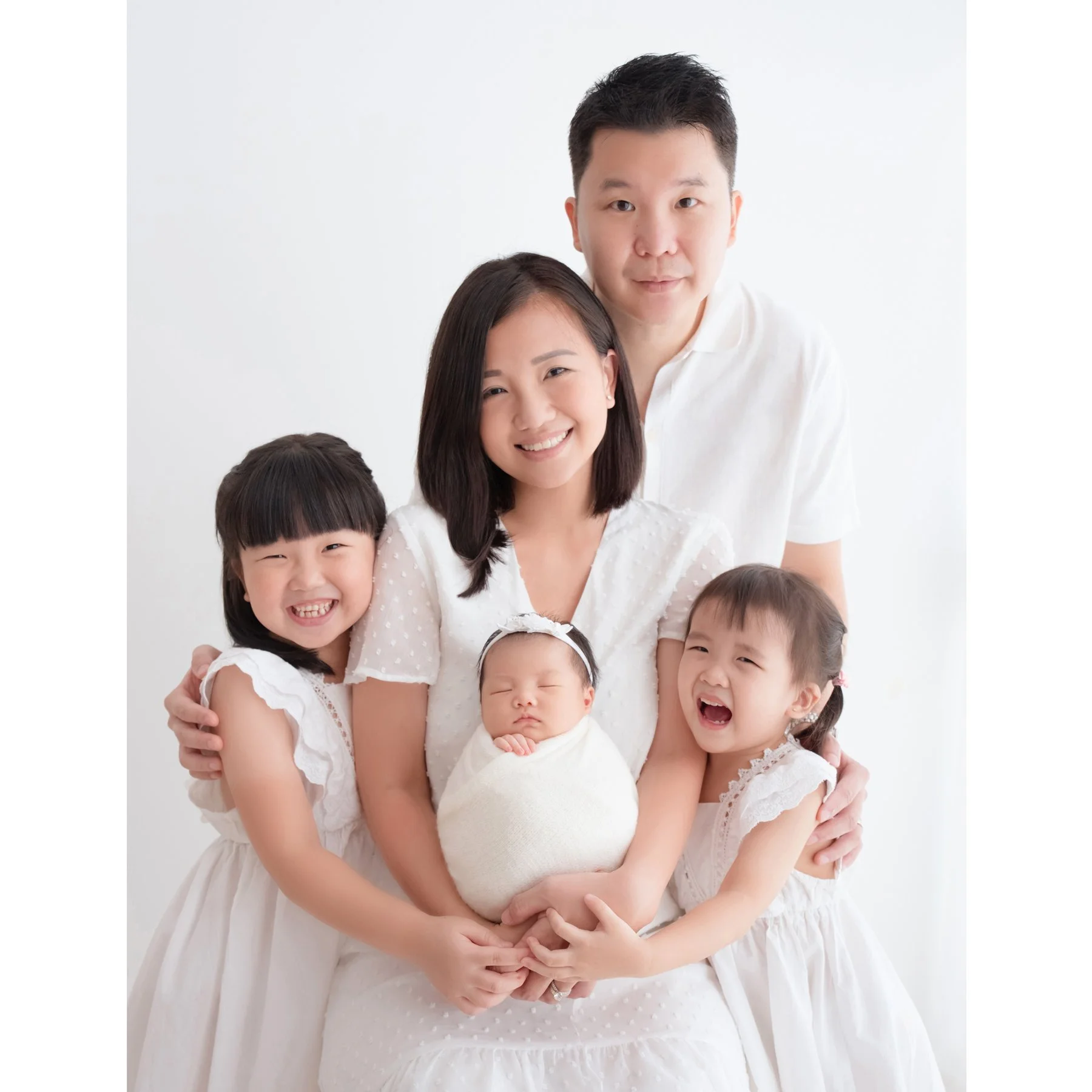 Family of five in white outfits holding a newborn between two older sisters