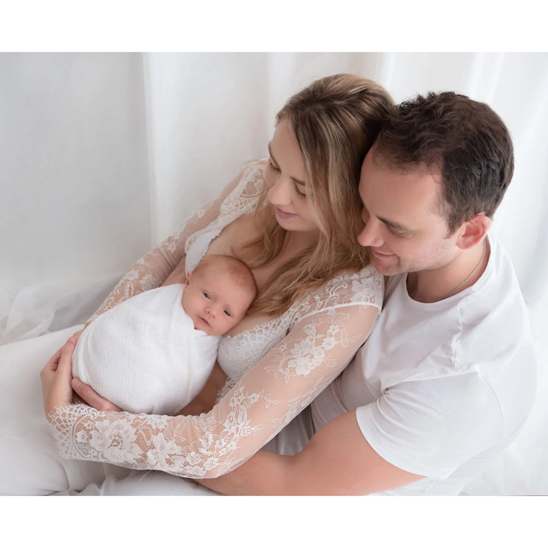 Parents gazing lovingly at their newborn wrapped in white, photographed from above