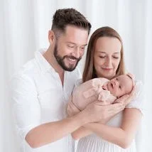 Smiling parents holding their sleeping newborn together against a white backdrop