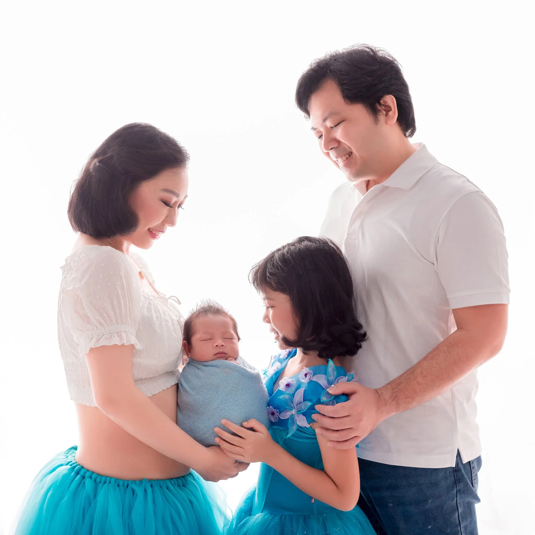 Parents and older sister gazing at their newborn wrapped in blue