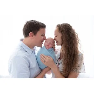 Parents kissing their newborn wrapped in blue against a bright white background