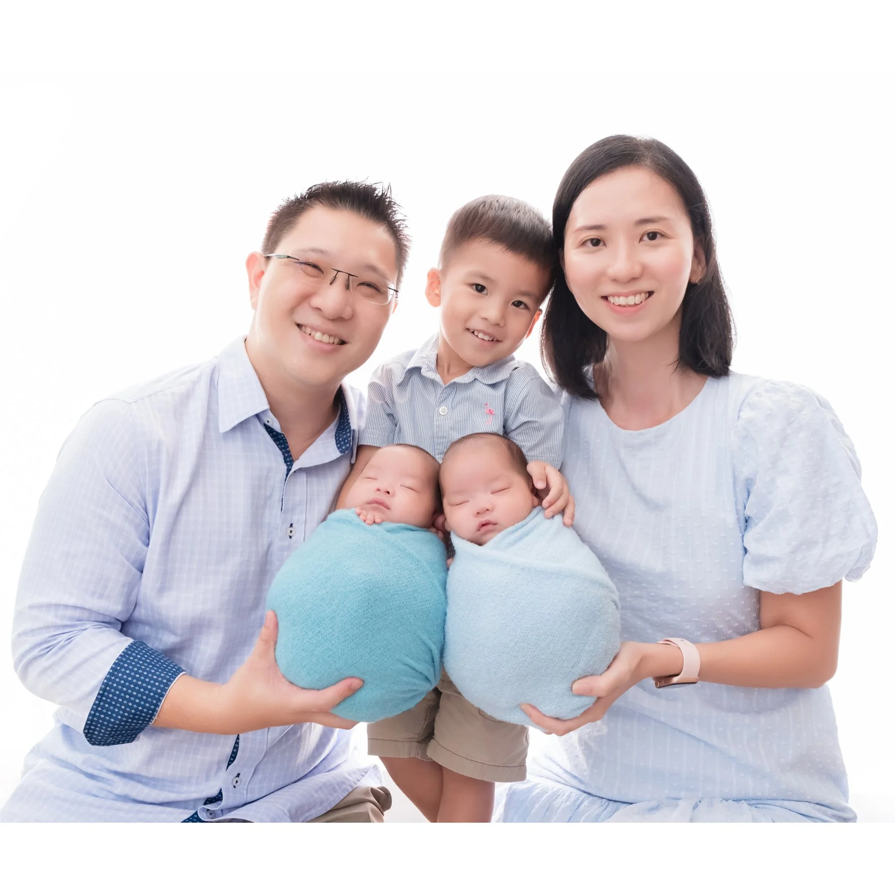 Parents holding their swaddled newborn twins with an older brother between them