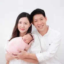 Smiling parents in white holding their newborn wrapped in pink