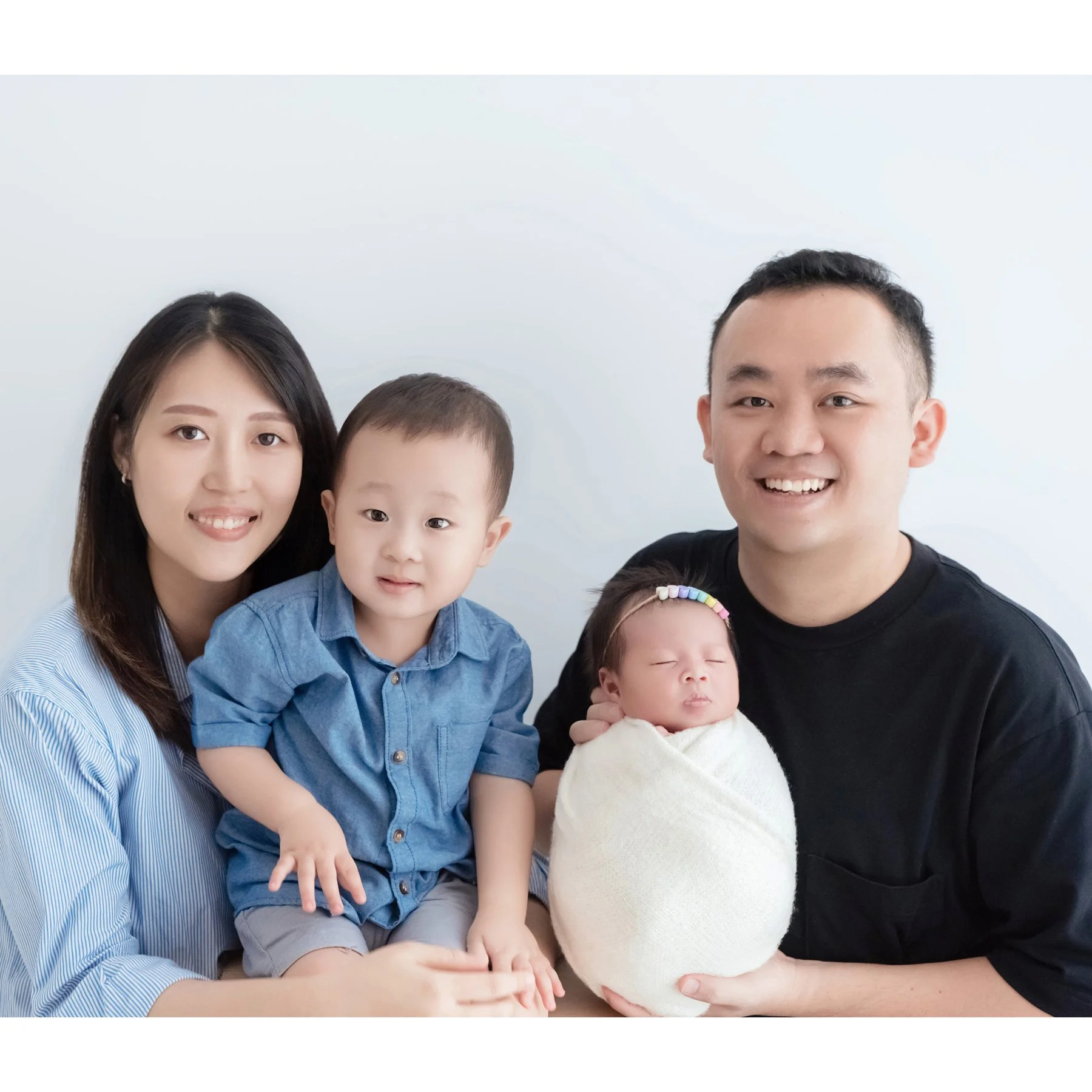 Parents and older brother smiling with their newborn wrapped in white