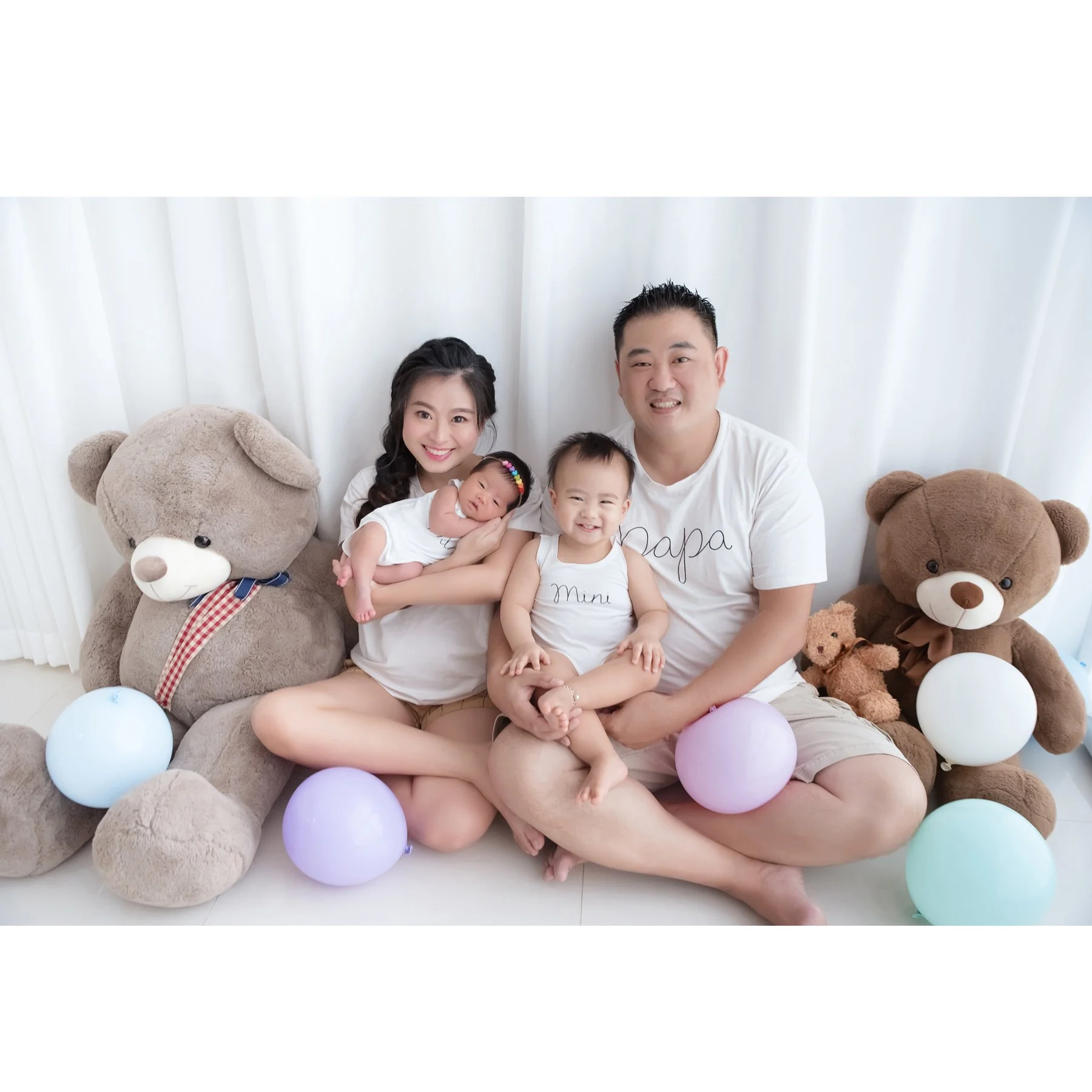 Family with an older sister and newborn seated among teddy bears and pastel balloons