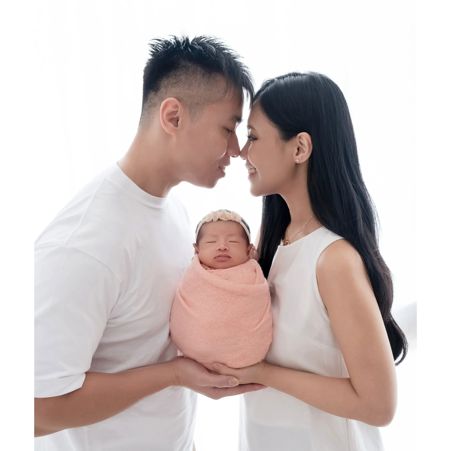 Parents kissing while cradling their newborn wrapped in pink
